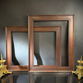 Two wooden picture frames on a reflective surface with a dark background