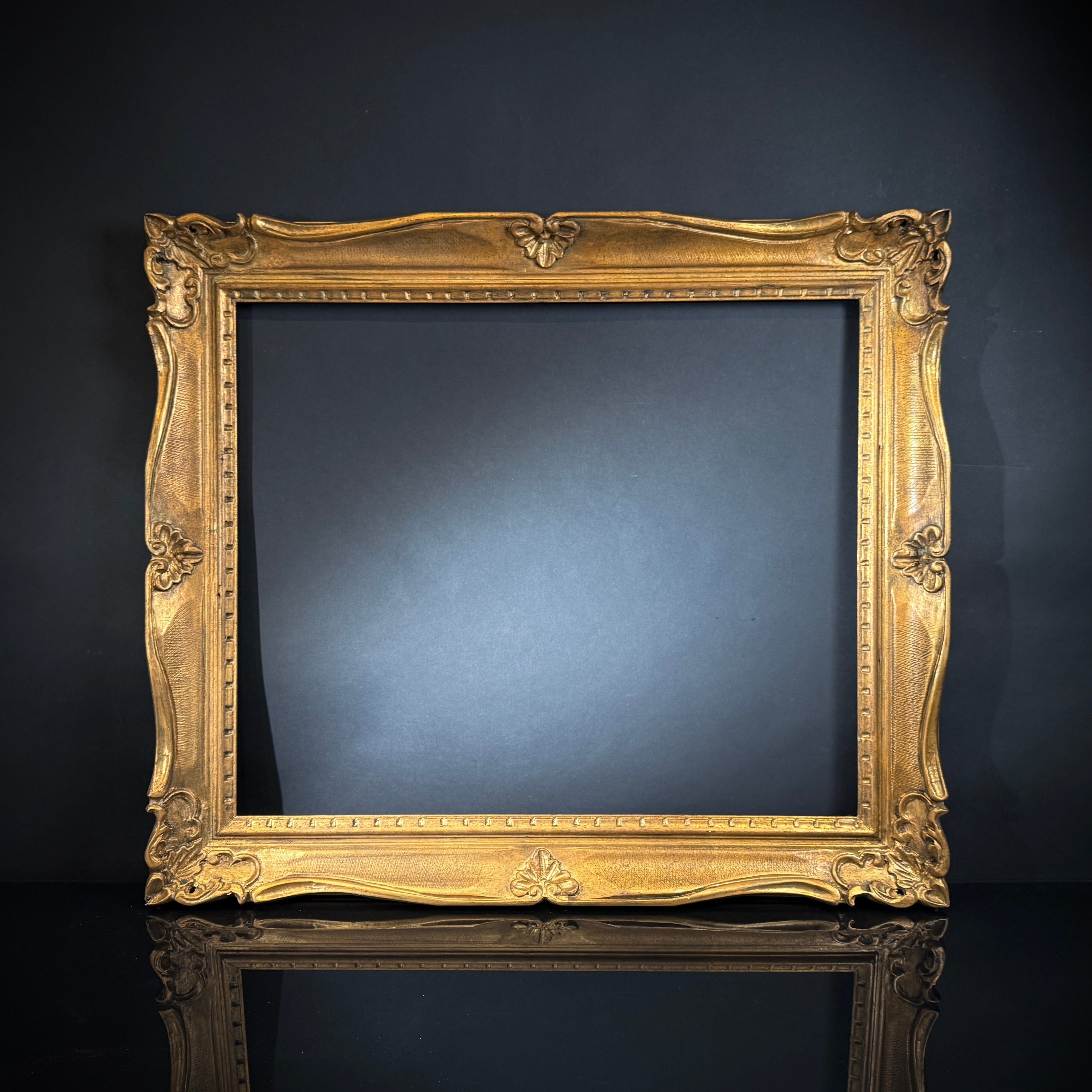 A large ornate carved gilt wood French vintage picture frame without a backing, displayed against a dark background.
